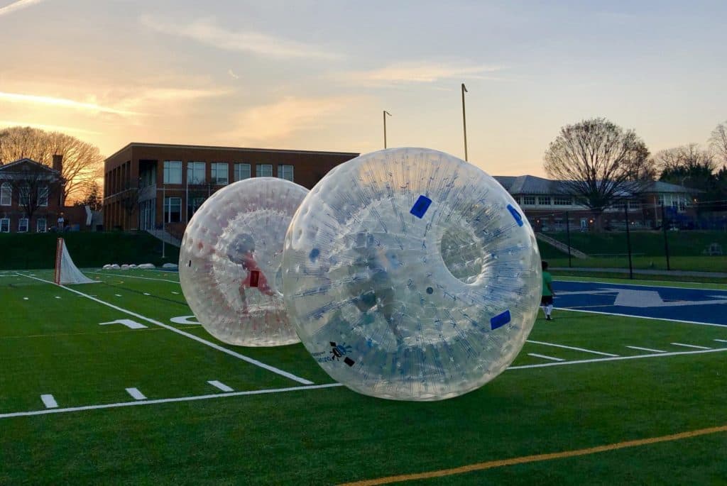 Personnes dévalant une pente herbeuse dans une boule de zorbing transparente